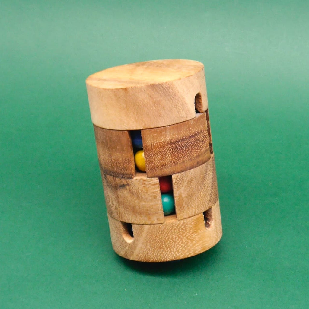 Leicht schräg positioniertes Holzpuzzle in Zylinderform, dessen versetzte Schlitze bunte Kugeln (Gelb, Blau, Rot, Türkis) preisgeben.