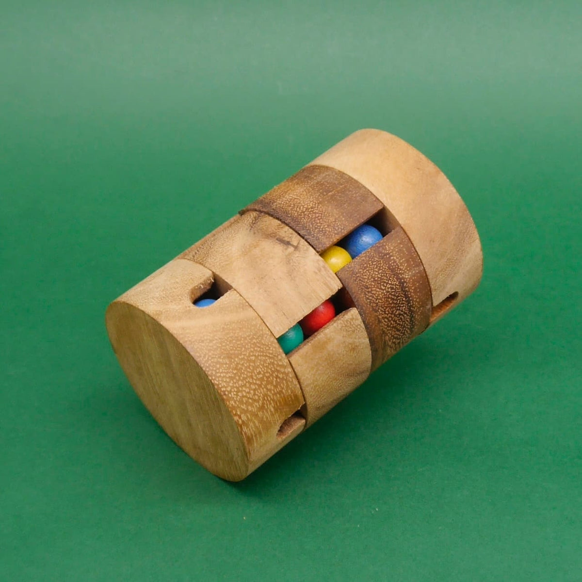 Seitlich liegendes Holz-Geduldspiel in Zylinderform; unterschiedlich farbige Kugeln sind durch zwei lange Schlitze sichtbar