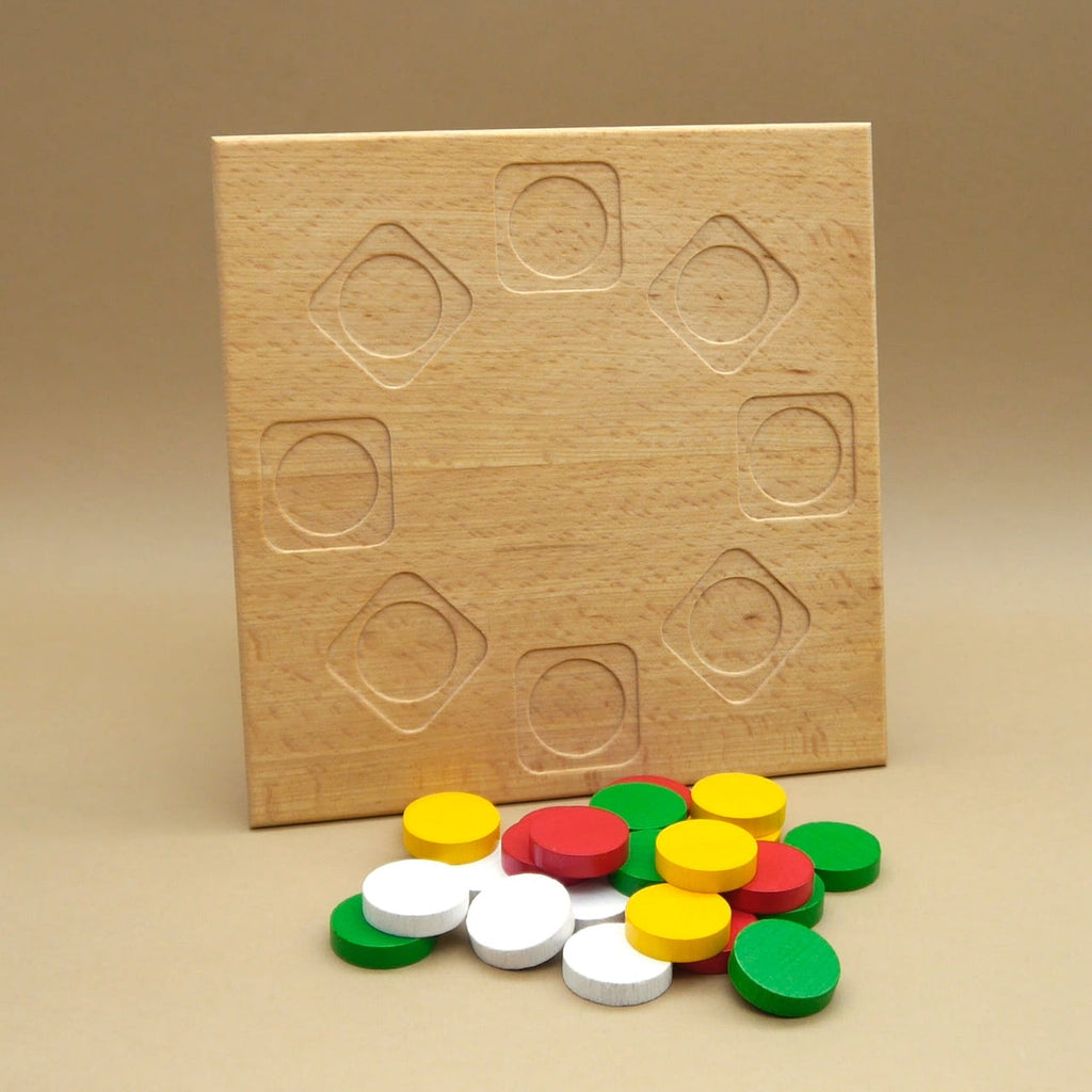 Rincala Geschenk: Holzbrett mit kreisförmigen Vertiefungen, davor lose bunte Spielsteine in Rot, Gelb, Grün und Weiß.