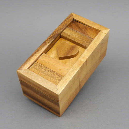 Holz-Schatztruhe mit Herzmotiv als verschließbares Denkspiel vor grauem Hintergrund.