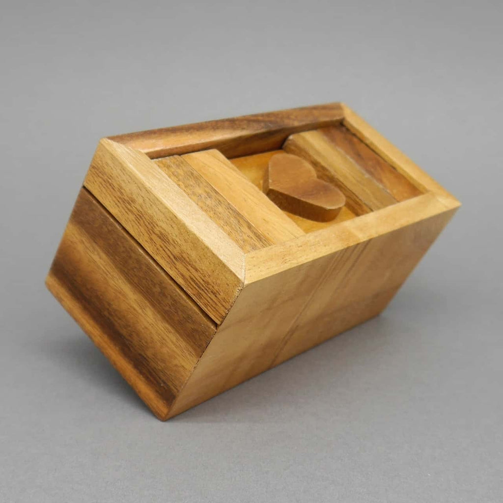 Schräg liegende Knobelbox aus hellem Holz, geschlossen, Herzschieber sichtbar oben auf dem Deckel.