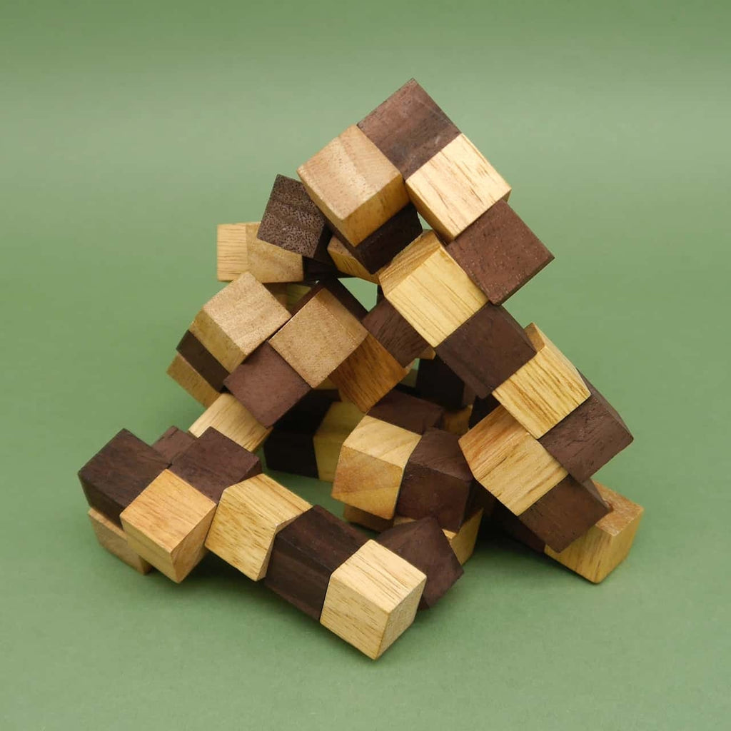 Teilzerlegter Brainteaser aus abwechselnd hellen und dunklen Holzwürfeln, pyramidenförmig aufgestellt vor grünem Hintergrund.