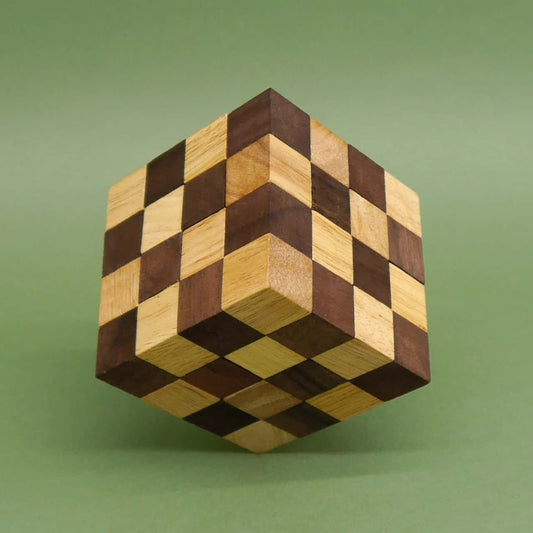 Perfekt zusammengesetzter Würfel als Denkspiel, schachbrettartig gemustert aus zweifarbigen Holzwürfeln, scheinbar schwebend über grünem Untergrund.