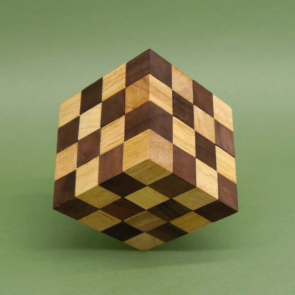 Perfekt zusammengesetzter Würfel als Denkspiel, schachbrettartig gemustert aus zweifarbigen Holzwürfeln, scheinbar schwebend über grünem Untergrund.