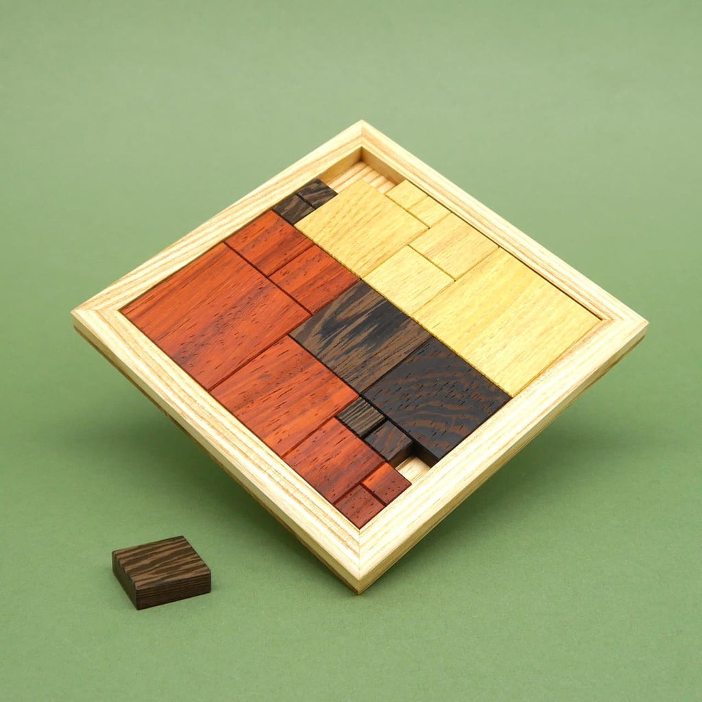 Ein vollständig zusammengesetztes Holzpuzzle aus verschiedenfarbigen Quadraten in einem Holzrahmen, schräg aufgestellt. Ein einzelnes Teil liegt davor.
