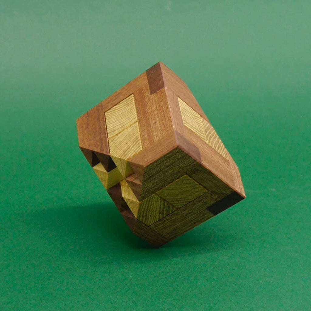 Ein komplexes Holzpuzzle aus verschiedenfarbigen Holzelementen, das leicht geneigt auf einer grünen Fläche balanciert.