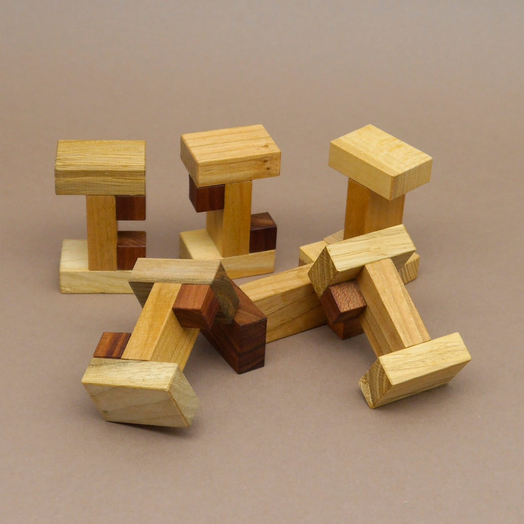 Mehrere auseinandergebaute Sixi Cube Brainteaser Holzteile liegen gruppiert auf einer neutralen Fläche; die gedrechselten Holzmodule in hellen und dunklen Tönen zeigen das Denkspiel, ideal als Geschenk für Rätselfans.