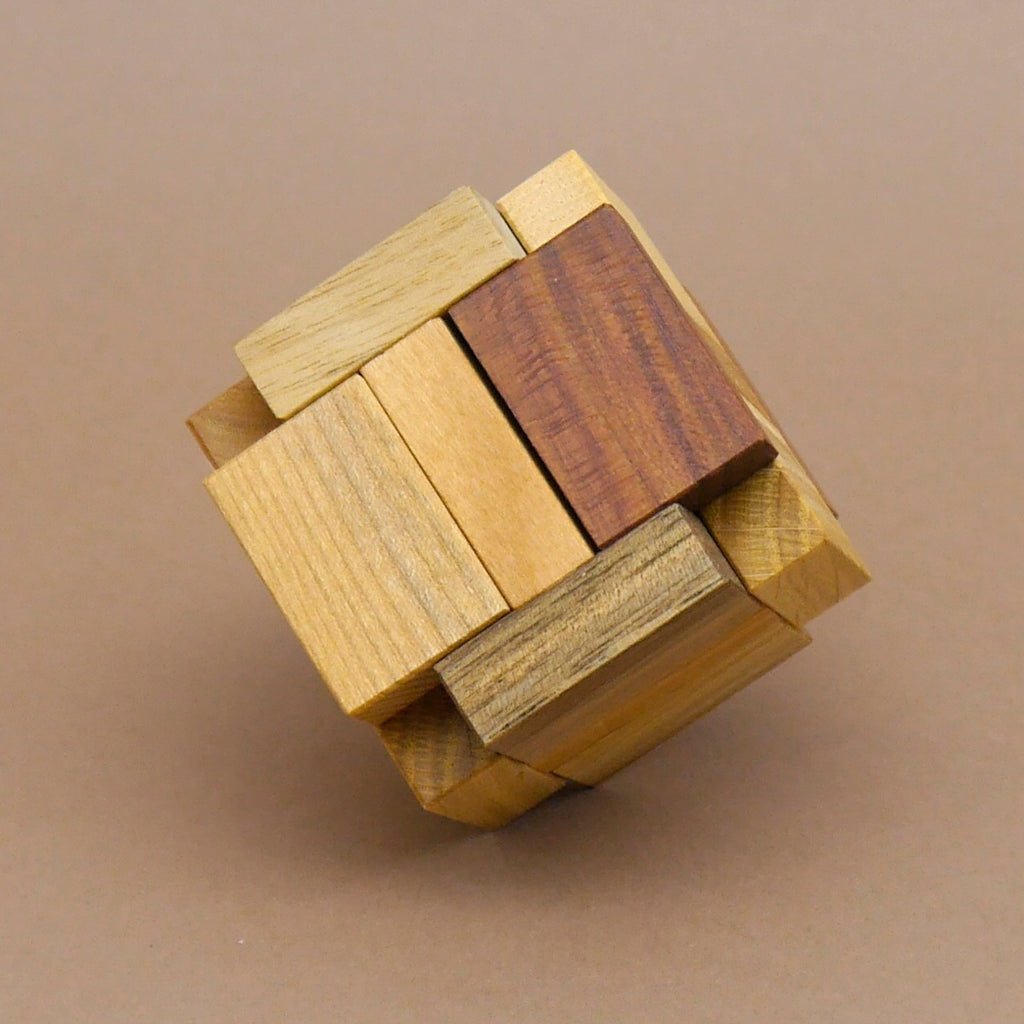 Kartonverpackung mit der Aufschrift Sixi Cube neben mehreren Einzelteilen des Knobel-Denkspiels aus Holz, präsentiert als Gehirntraining-Puzzle für Erwachsene.