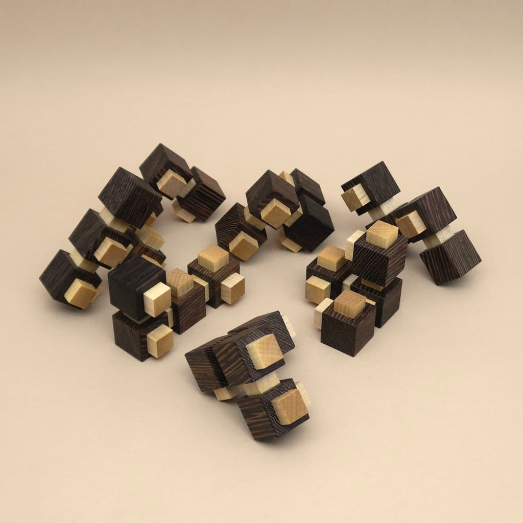 Mehrere zerlegte Holzelemente eines dunklen und hellen 3D-Puzzles liegen auf beigem Hintergrund, bereit zum Zusammensetzen zu einem Würfel.