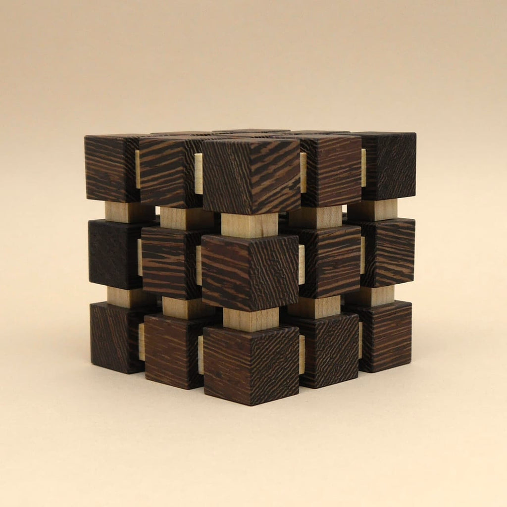 Perspektivisch fotografierter, sauber aufgebauter Holzwürfel mit dunklen Außenwürfeln und hellen Verbindern als Geduldsspiel.