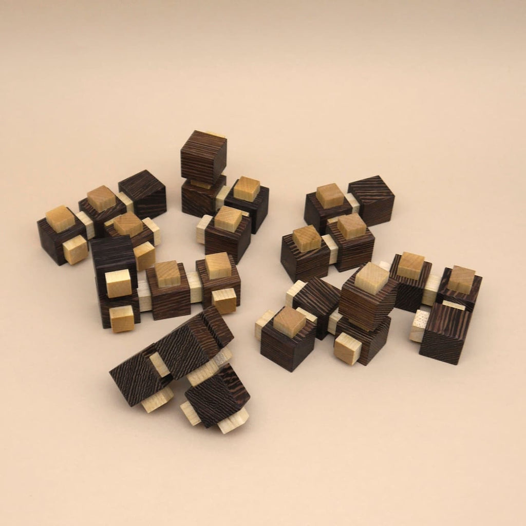 Auf beigem Untergrund verstreute modulare Holzwürfel-Teile eines logischen Knobelspiels, die zu einem größeren Würfel verbunden werden können.