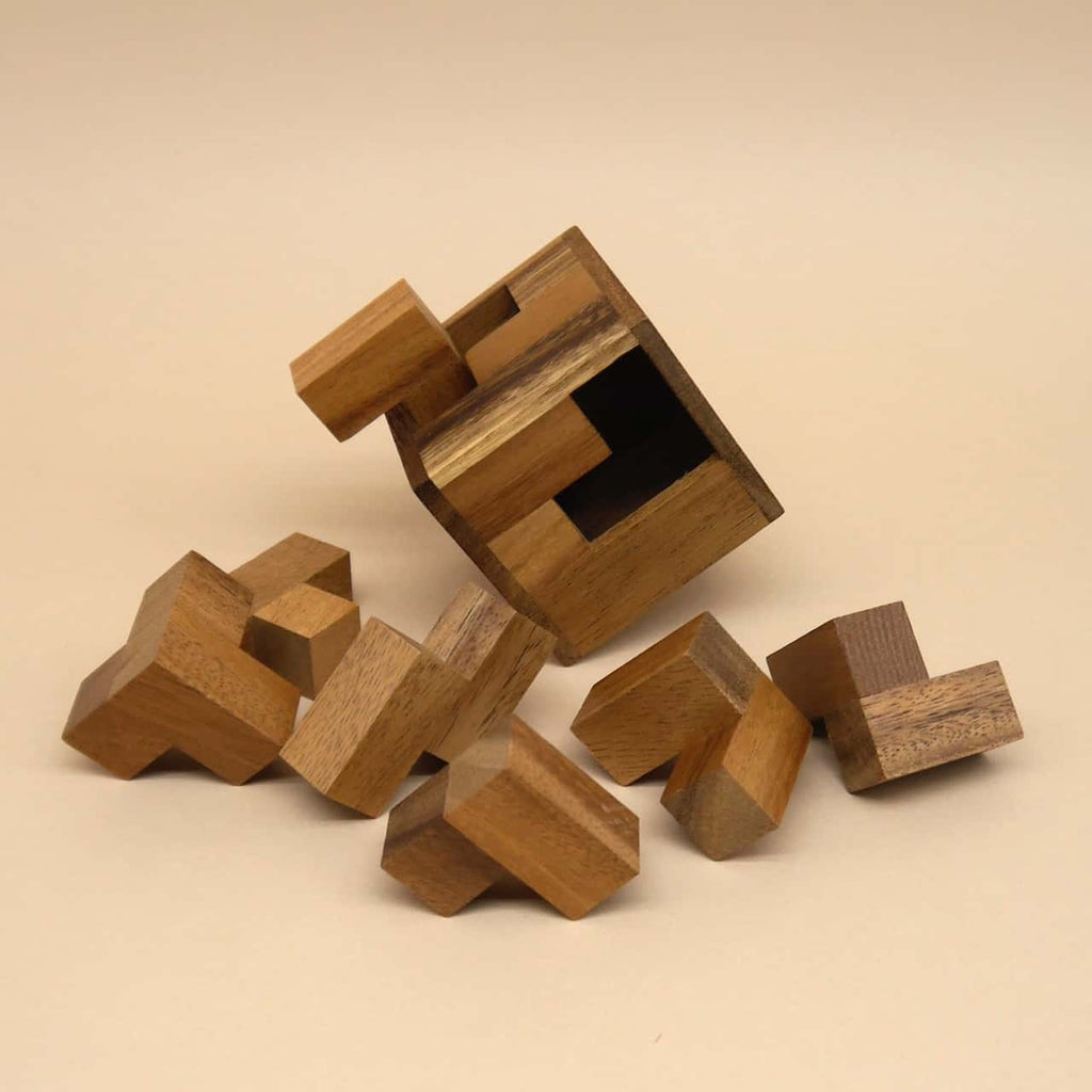 Auseinandergefallene Holzpuzzle-Teile rund um einen leeren Würfel auf hellem Hintergrund.