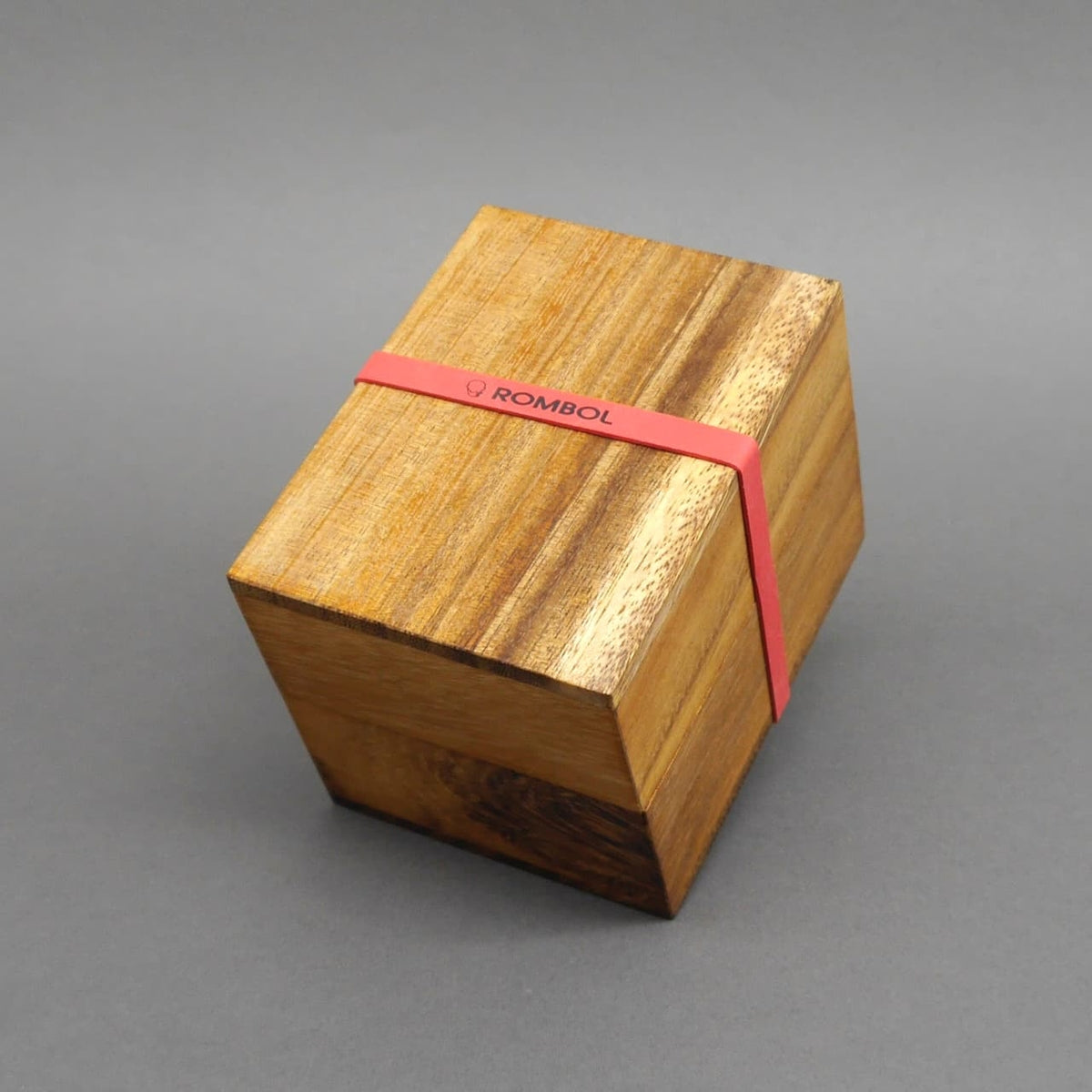 Holzwürfel-Puzzle in geschlossener Holzbox mit rotem Gummiband, ideal als Denkspiel für Knobelfreunde.