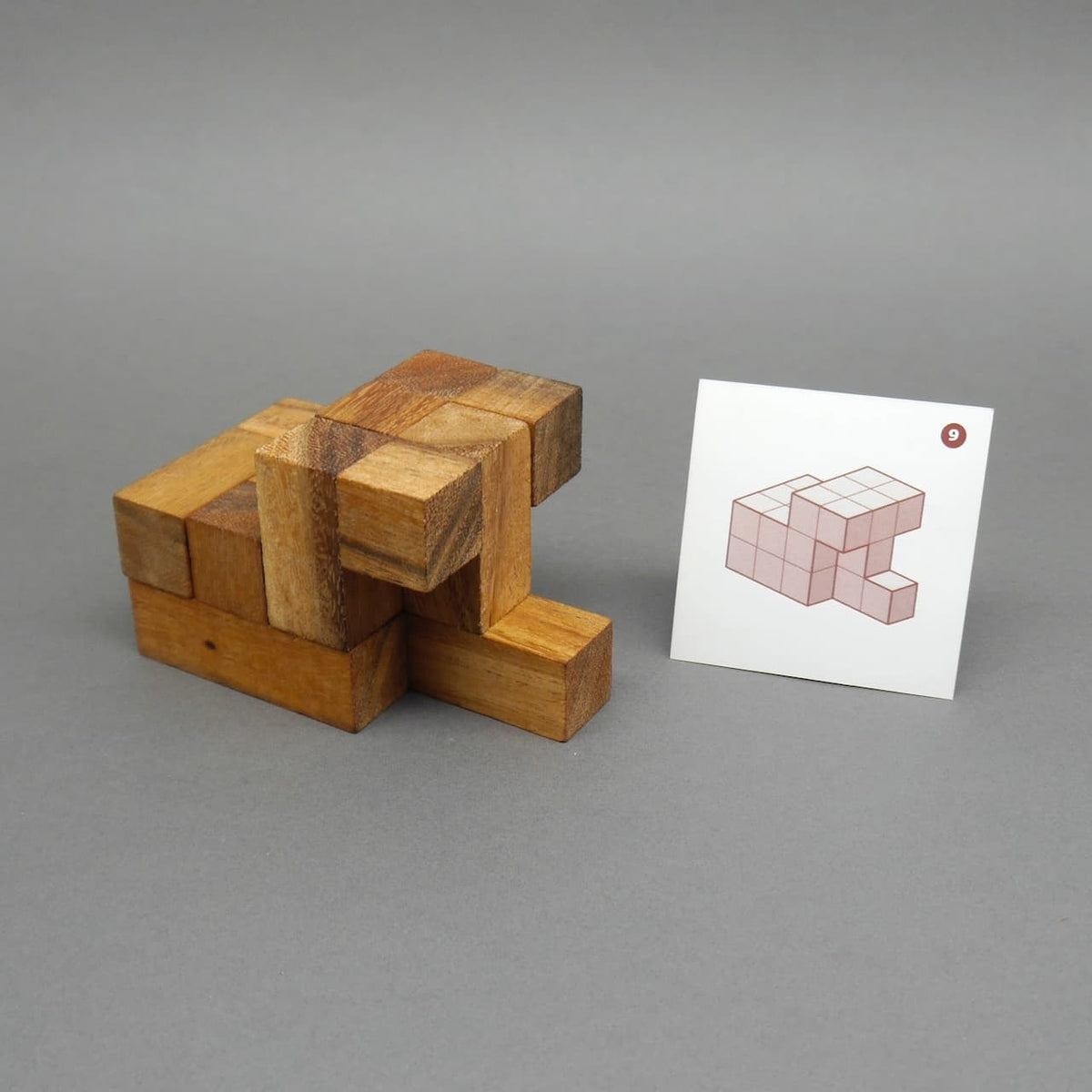 Teilweise zusammengesetztes Soma-Würfel-Geduldsspiel neben einer Lösungskarte mit Tangram-ähnlicher Aufgabe.