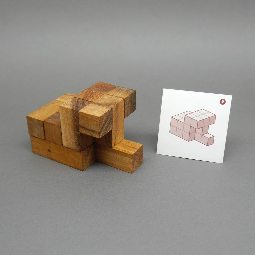 Teilweise zusammengesetztes Soma-Würfel-Geduldsspiel neben einer Lösungskarte mit Tangram-ähnlicher Aufgabe.