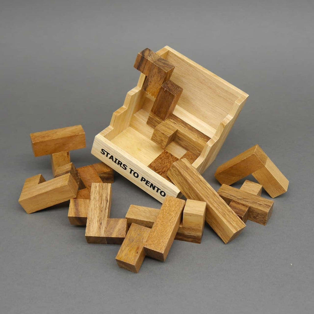 Das Logikpuzzle „Stairs to Pento“ liegt offen, während zahlreiche winkelige Pentomino-Steine verstreut auf grauem Untergrund liegen.