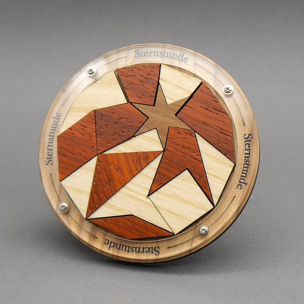 Aufrecht stehendes Knobelspiel ‚Sternstunde‘: rundes Holz-Packing-Puzzle mit Stern aus hellen und rötlichen Segmenten.