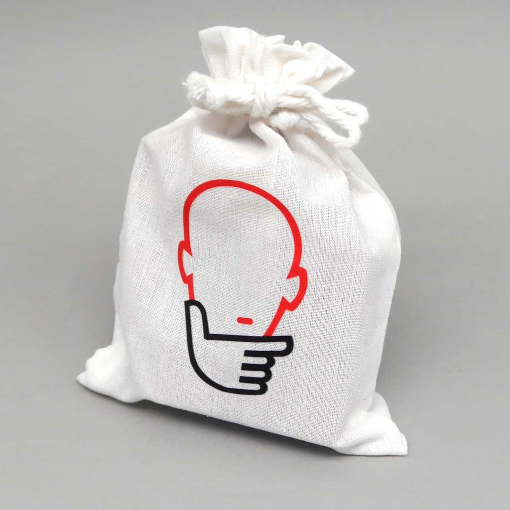 Weißer Stoffbeutel mit minimalistischem Gesichtspiktogramm enthält ein hölzernes Logikpuzzle.