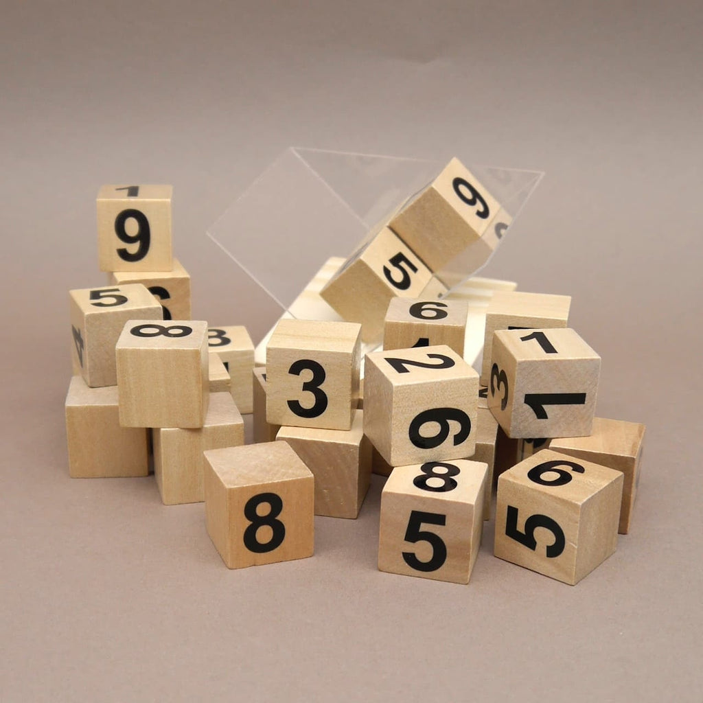 Holzwürfel mit schwarzen Zahlen liegen als Knobelspiel verstreut auf einer neutralen Fläche.