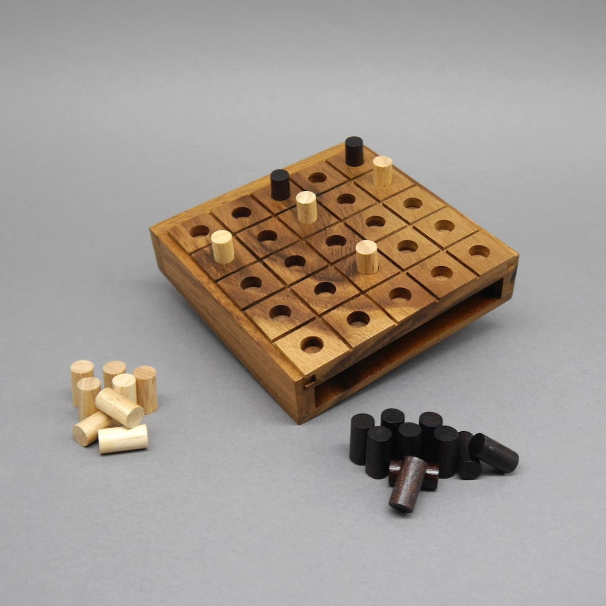 Holz-Strategiespiel „Switch“: 5 × 5-Brett mit runden Löchern, helle und dunkle Stifte liegen spielbereit daneben.