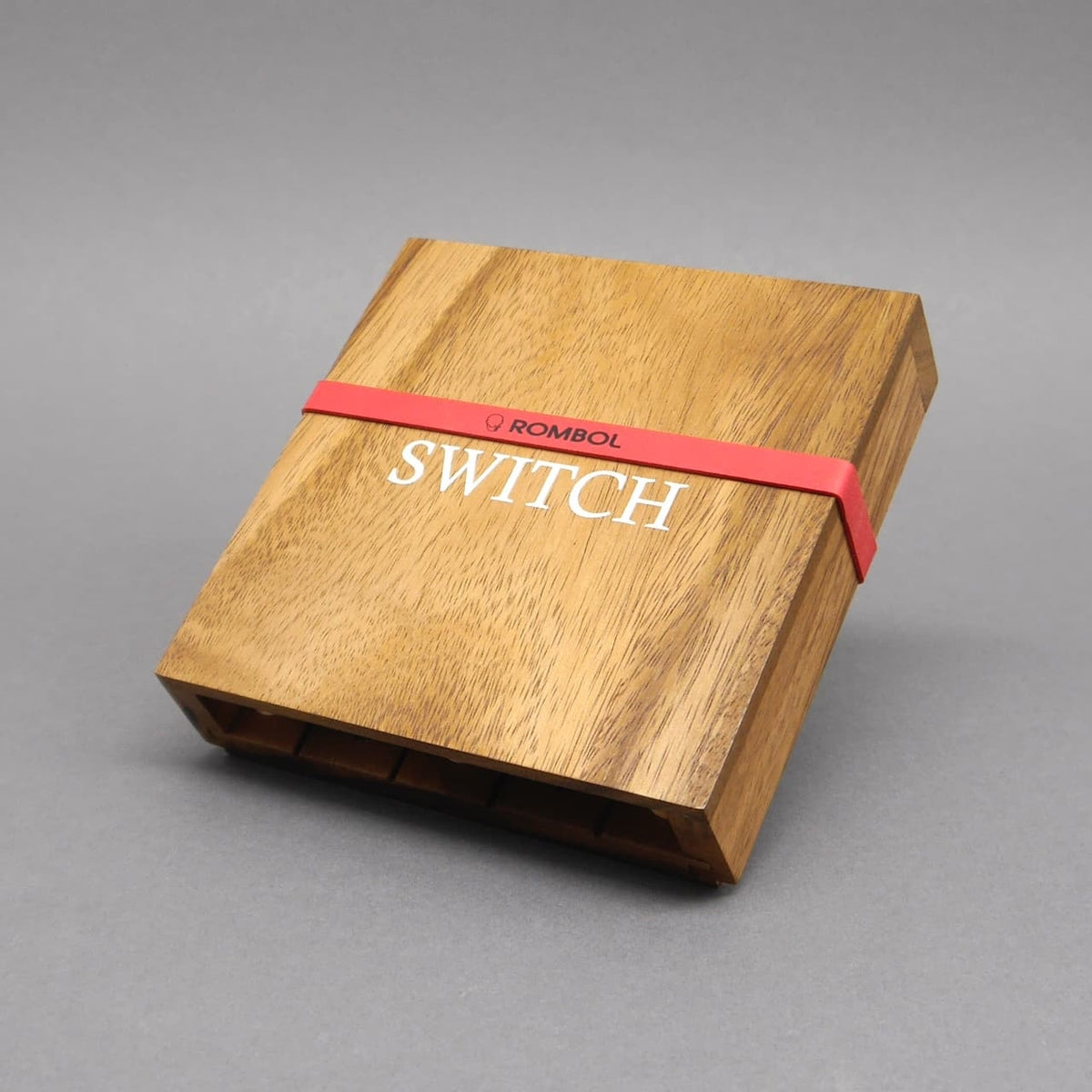 Geschlossene Holzbox des Holzspiels „Switch“ mit rotem Gummiband und weißem Schriftzug auf dem Deckel.
