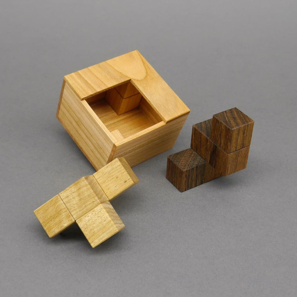 Offene Holzkiste mit zwei geometrischen Holzformen daneben, die als Teile eines kniffligen Denkspiels dienen.