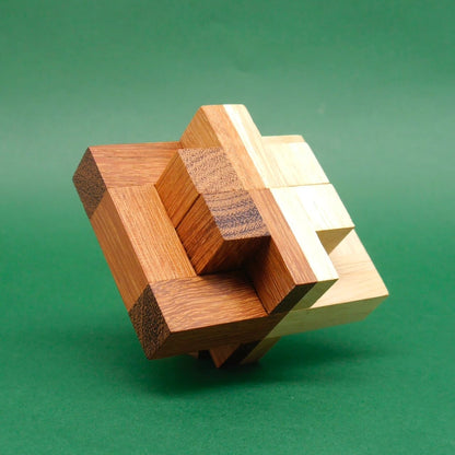 Schräg aufgestelltes Holz-Geduldspiel in sternförmiger Würfelstruktur aus hellen und dunklen Quadern vor grünem Hintergrund.