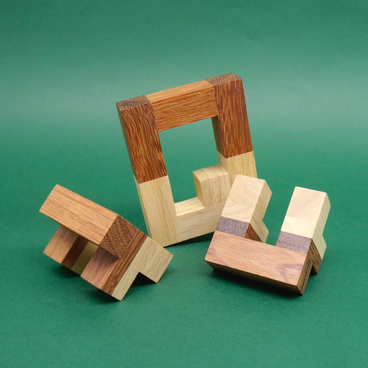 Zerlegtes Logikpuzzle aus hellen und dunklen Holzklötzen; ein rechteckiger Rahmen und zwei Winkelteile liegen auf grünem Untergrund.