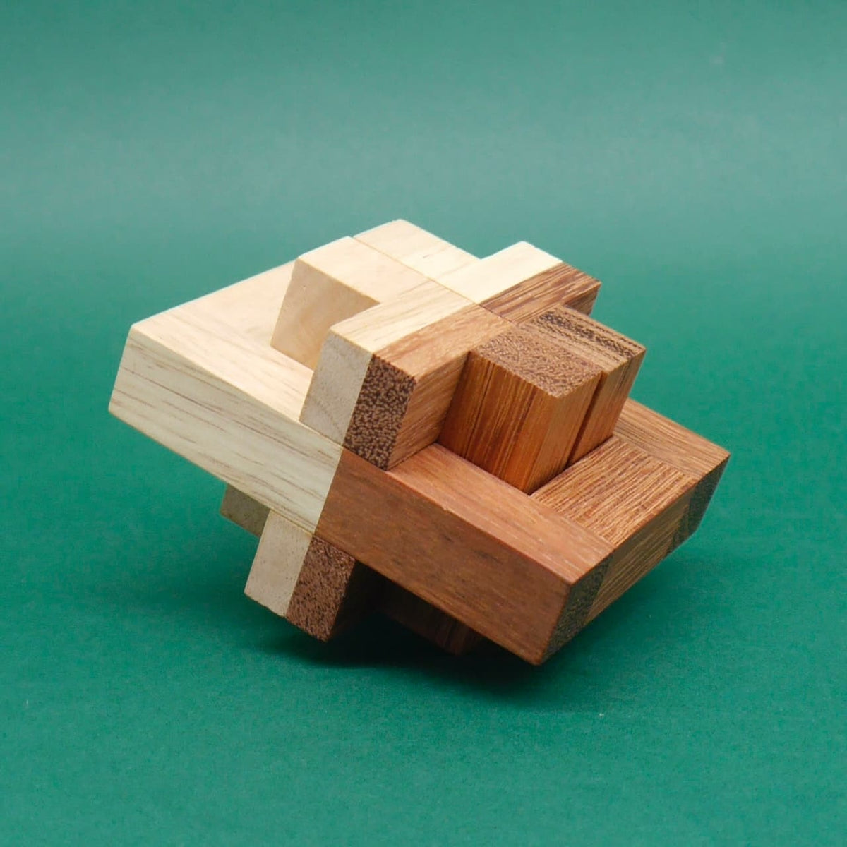 Komplexes Holzpuzzle aus unterschiedlich farbigen Quadern, fertig zusammengesetzt und leicht gekippt vor grünem Hintergrund.