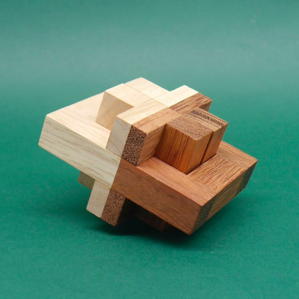 Komplexes Holzpuzzle aus unterschiedlich farbigen Quadern, fertig zusammengesetzt und leicht gekippt vor grünem Hintergrund.