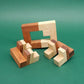 Auseinandergelegtes IQ-Puzzle aus zweifarbigem Holz; ein rechteckiger Rahmen und vier L-förmige Module liegen auf grünem Filz.