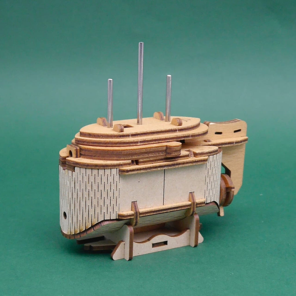 Trickbox Tesla’s Boat: montierte Holzbox mit drei Metallstiften und feinen Gravuren auf grünem Hintergrund.