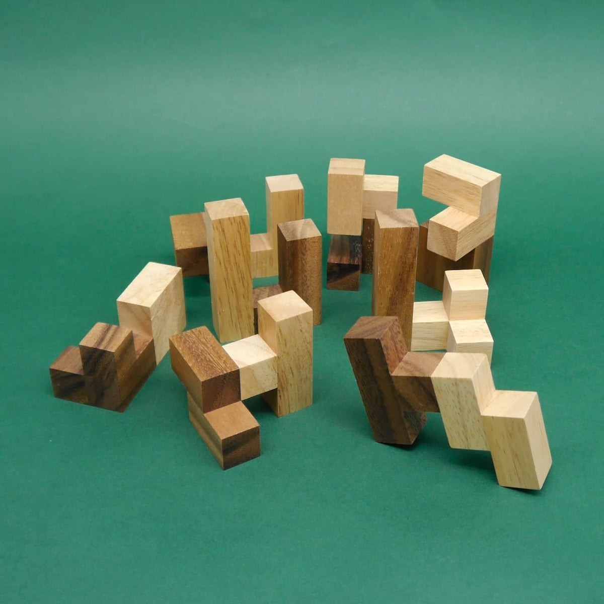 Einzelne verzahnte Holzbausteine eines Logikpuzzle liegen auseinandergebaut auf grüner Fläche.