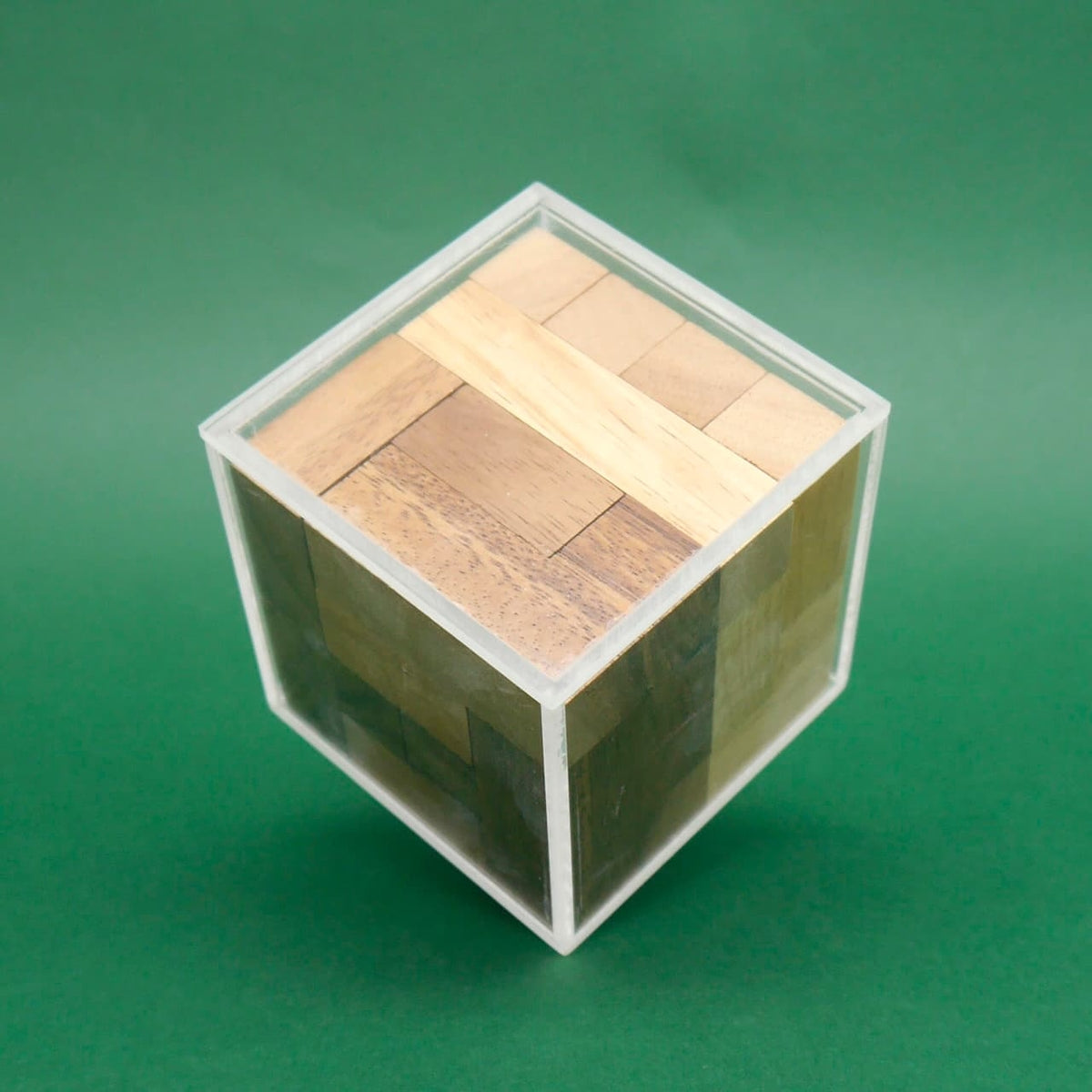 Vollständig zusammengesetztes Holzpuzzle steckt passgenau in einer transparenten Kunststoffbox vor grünem Hintergrund.