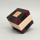 Knobelspiel in Form eines Holzpuzzles aus dunklen, rötlichen und hellen Holzblöcken, perfekt zu einem Würfel gefügt.
