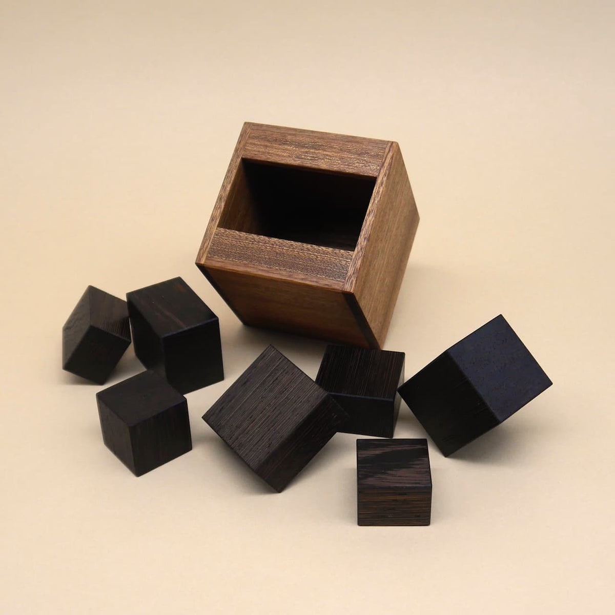 Offene Holzkiste mit mehreren schwarzen Würfeln, die Teil eines Denkspiels zum Knobeln sind.