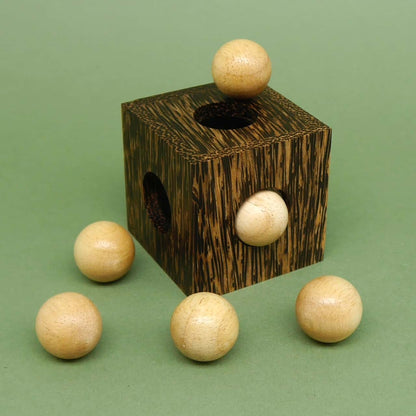 Holzwürfel mit einer Kugel obenauf und weiteren fünf Kugeln rundherum – kreatives Packpuzzle, das räumliches Denken fordert.