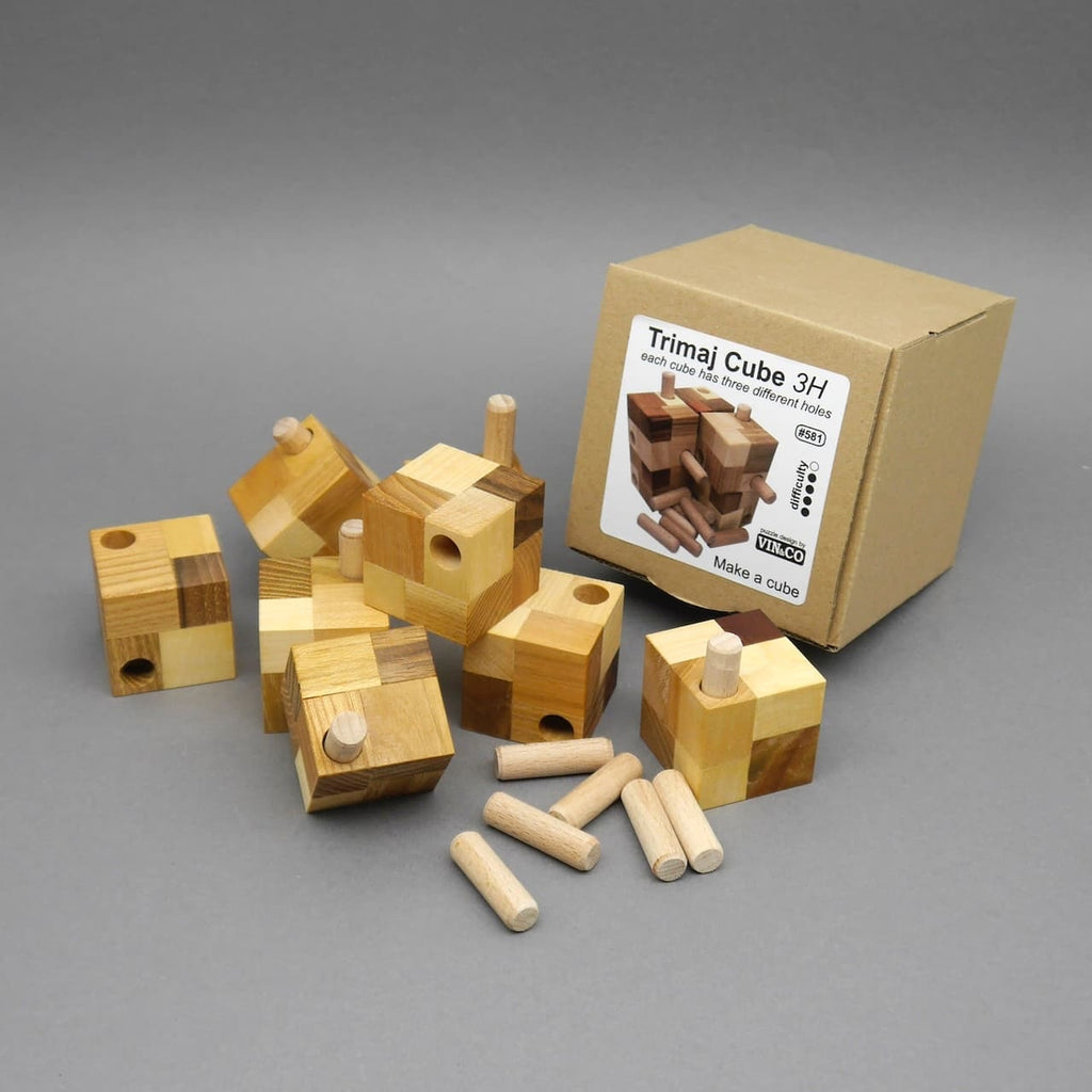 Mehrere kleine Holzwürfel des Trimaj Cube 3H mit Steckdübeln liegen vor der Kartonverpackung, als Knobelpuzzle zum Zusammenbauen eines großen Würfels dargestellt.