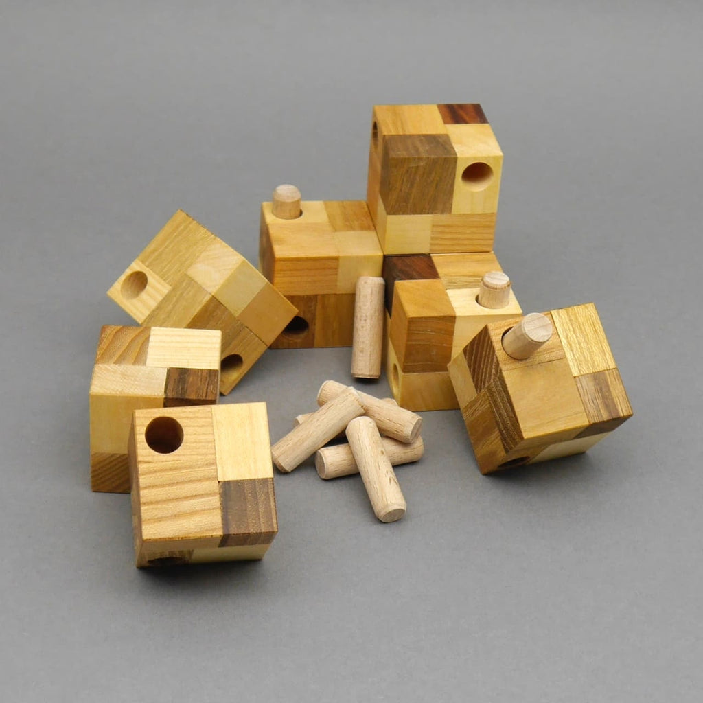 Einzelteile des Trimaj Cube 3H aus Holz – mehrere kleine Würfelmodule mit Bohrungen und Dübeln – als Knobelspiel ausgelegt auf grauer Fläche.