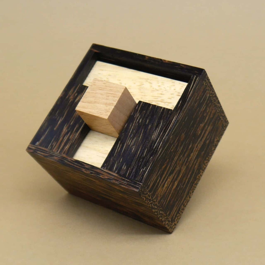 Holzpuzzle in Form eines dunklen Würfels mit hellen Einpass­stücken, komplett zusammengesetzt auf beigem Hintergrund.