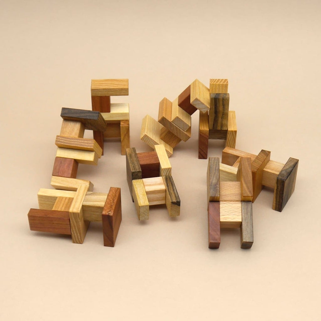 Einzelne Holzteile des Geduldspiels liegen in lockeren Gruppen auf einem neutralen Untergrund und zeigen die unterschiedlichen Formen des 3D-Puzzle.