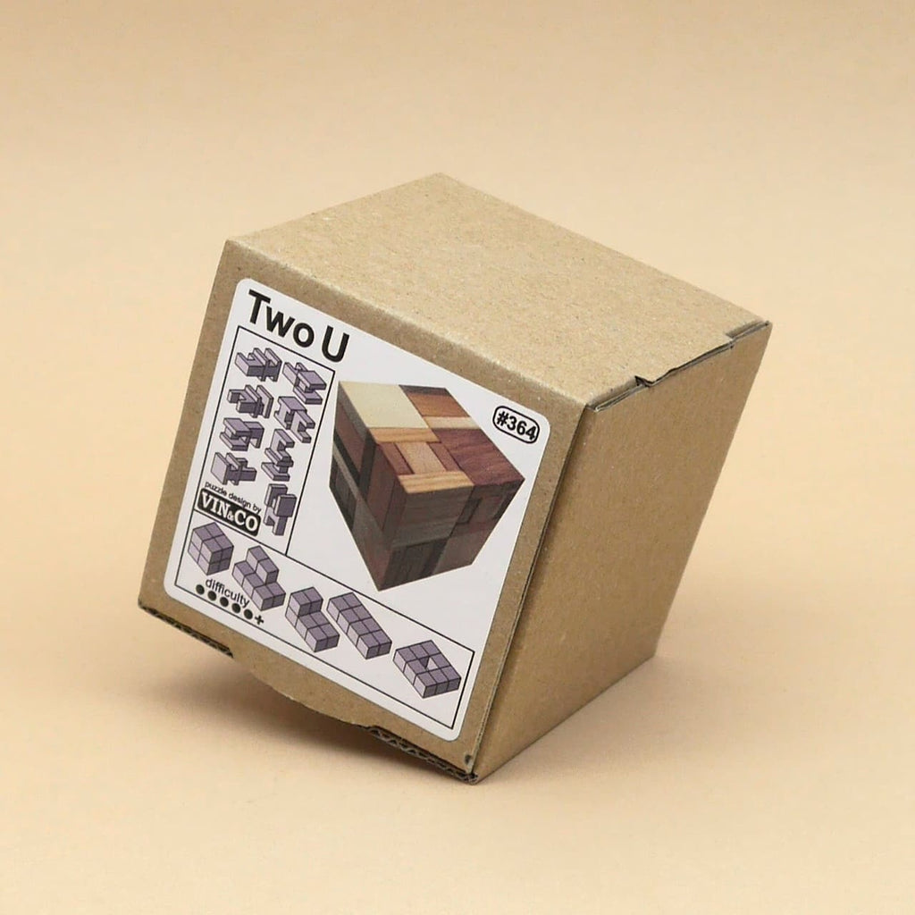 Schlichte Kartonverpackung des Denkspiels mit Aufkleber, der das fertige Woodenpuzzle als mehrfarbigen Holzwürfel zeigt.