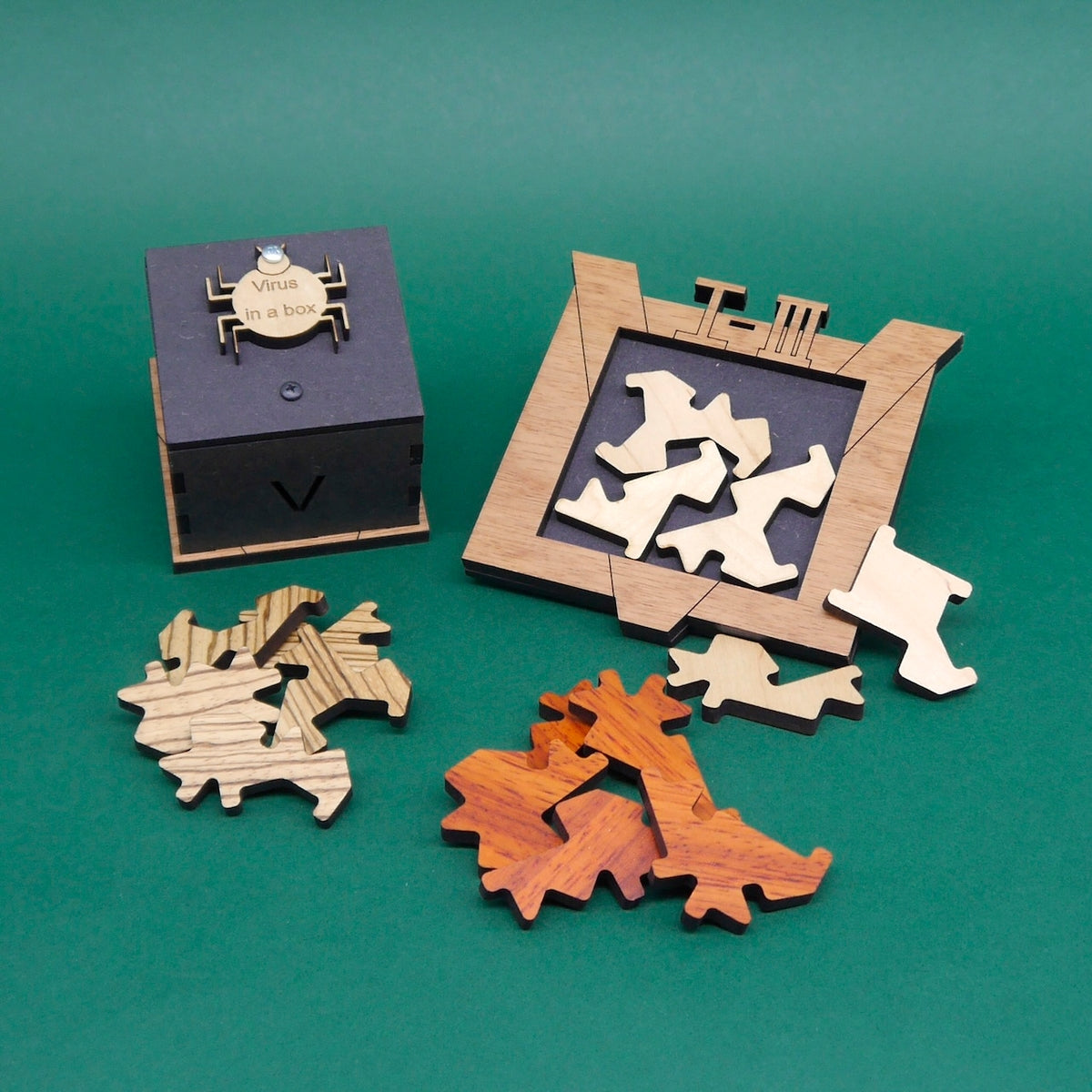 Dreiteiliges Holzpuzzle-Set „Virus in a Box“ mit einer geschlossenen Puzzlebox, einer Spielfläche mit eingelegten weißen Teilen und sortierten Puzzleteilen in drei Farben.