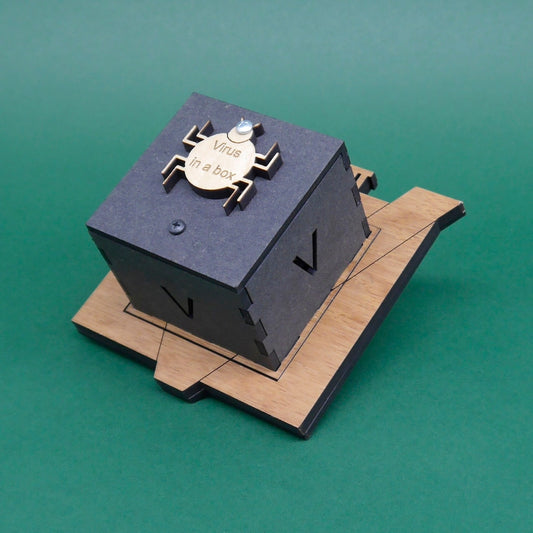 Zusammengebaute Puzzlebox „Virus in a Box“ auf Holzplattform mit graviertem Schriftzug und stilisierter Virus-Grafik auf dem Deckel.