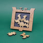 Holzrahmen mit eingelegten Puzzleformen in heller Maserung, zwei weitere Teile liegen davor – ein Logikspiel mit raffiniertem Design.