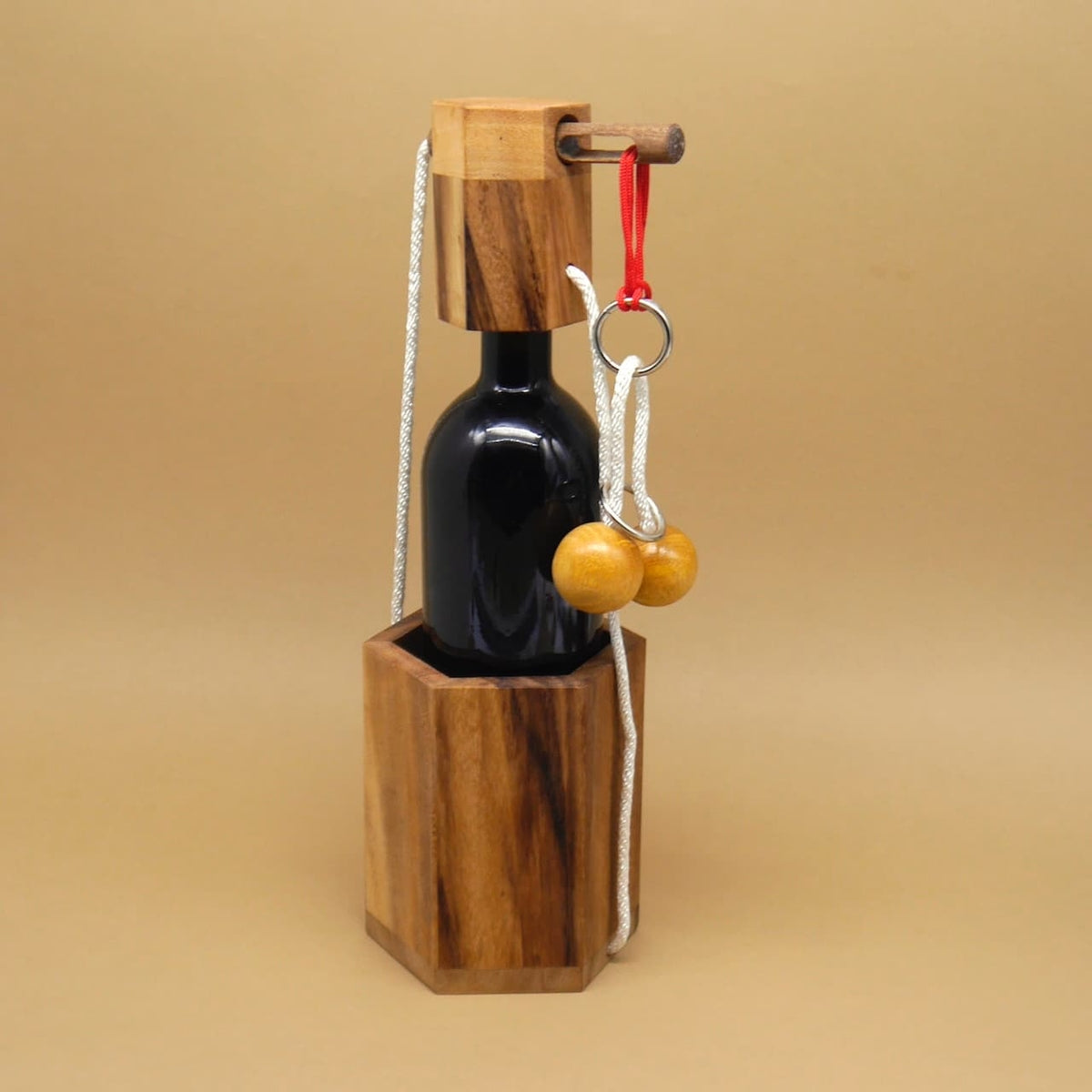 Aufgebautes Geduldspiel: Weintresor aus Holz mit Kordeln, Ringen und zwei Holzkugeln; sichert eine dunkle Weinflasche.