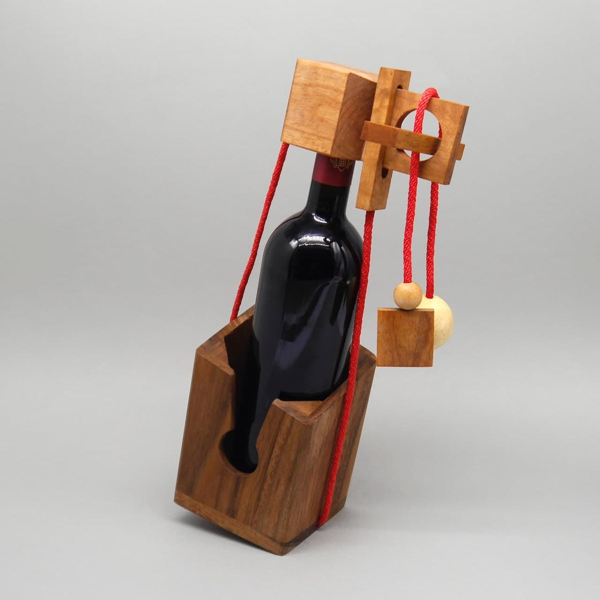 Flaschenverpackung als Knobelspiel: Weinflasche im Holzhalter mit roter Kordel – originelles Flaschengeschenk.