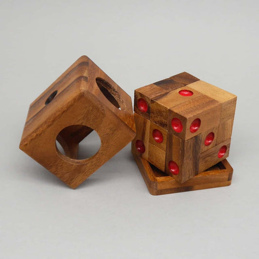 Ein fertig zusammengesetzter Holzwürfel als Denkspiel steht auf seiner Ablage, daneben die offene Außenbox – rote Mulden markieren die Würfelseiten.