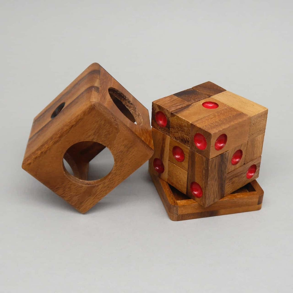 Ein fertig zusammengesetzter Holzwürfel als Denkspiel steht auf seiner Ablage, daneben die offene Außenbox – rote Mulden markieren die Würfelseiten.