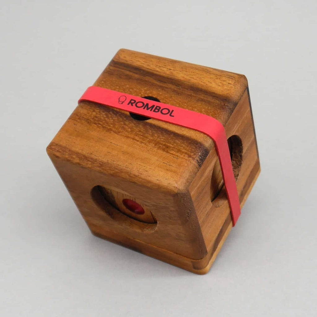 Das gelöste Knobelspiel aus Holz ist mit einem rotem ROMBOL-Gummiband gesichert und zeigt durch Öffnungen einen roten Punkt.
